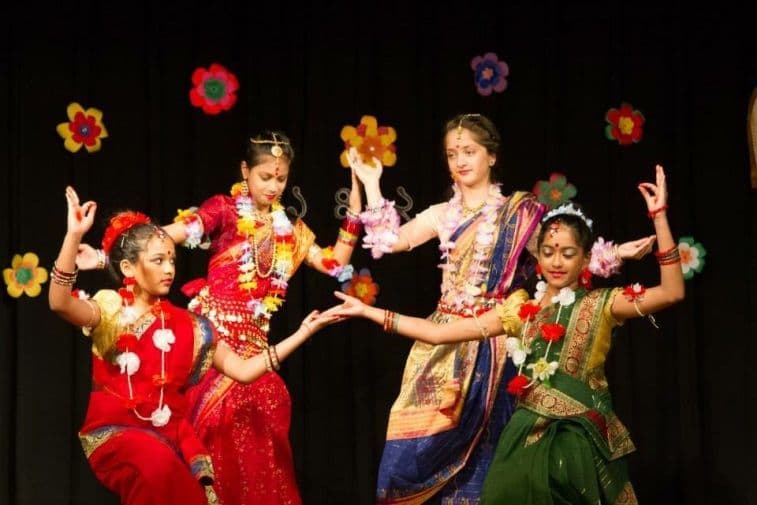 Four girls performing a classical dance in red, gold, and blue saris