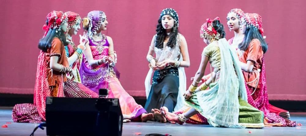 Young dancers in colorful costumes seated on stage during a dance drama