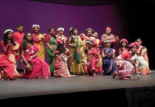 A large group of dancers holding a Bangladesh flag on stage