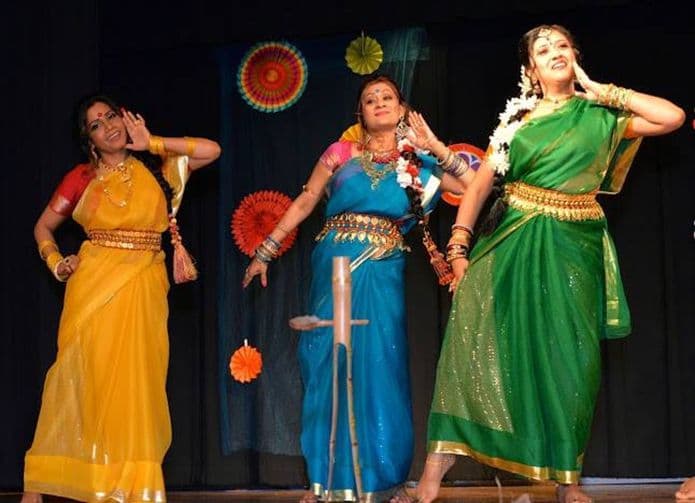 Three women dancing in yellow, blue, and green saris